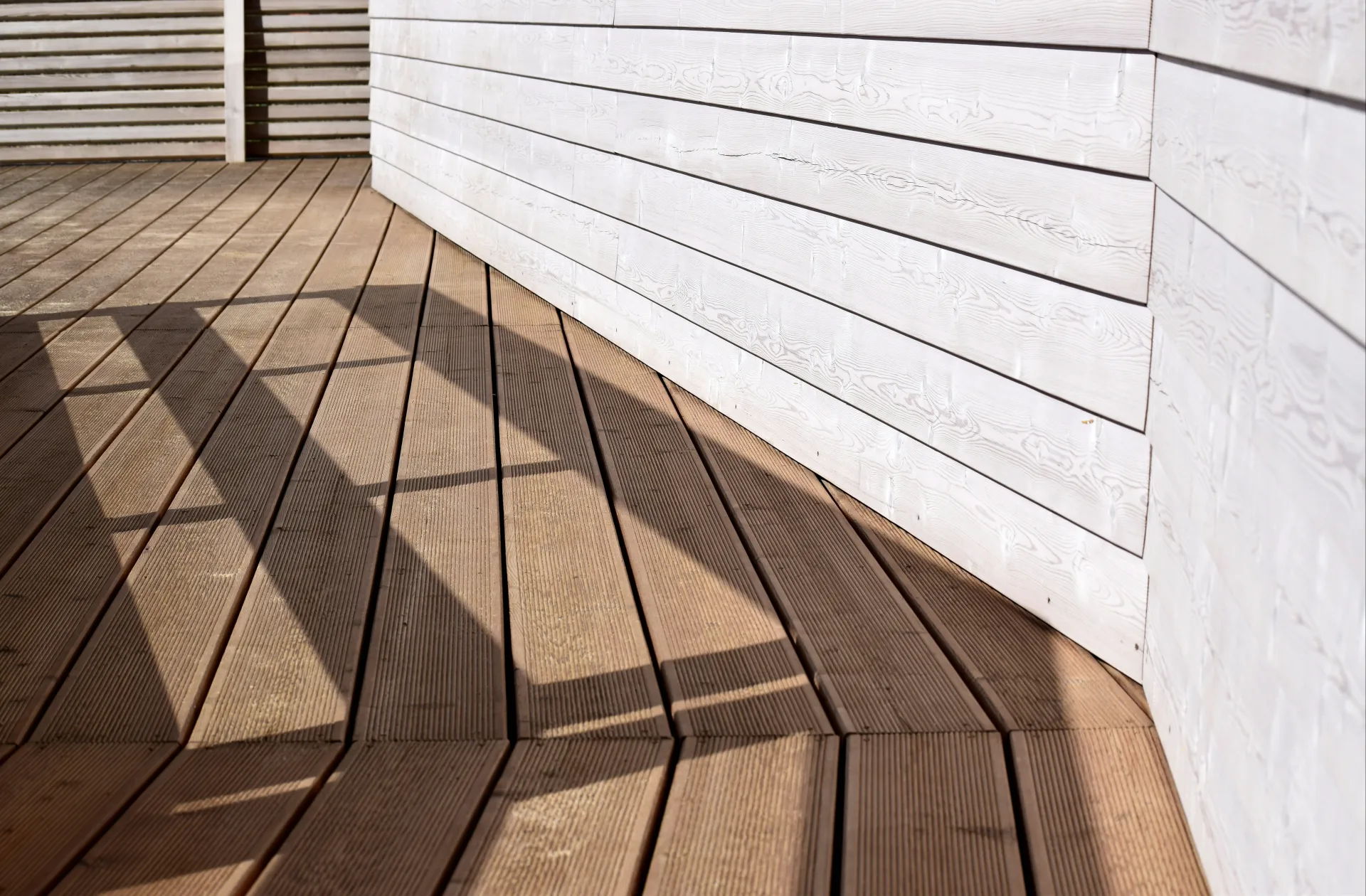 Nahaufnahme geriffelter Holzdielen einer Terrasse entlang einer hellen Holzwand