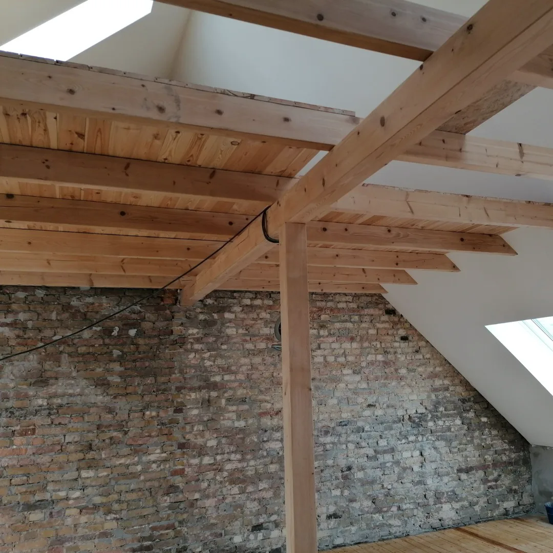 Ausgebautes Dachgeschoss mit sichtbaren Holzbalken, Ziegelwand, Dachfenstern und Dielenboden